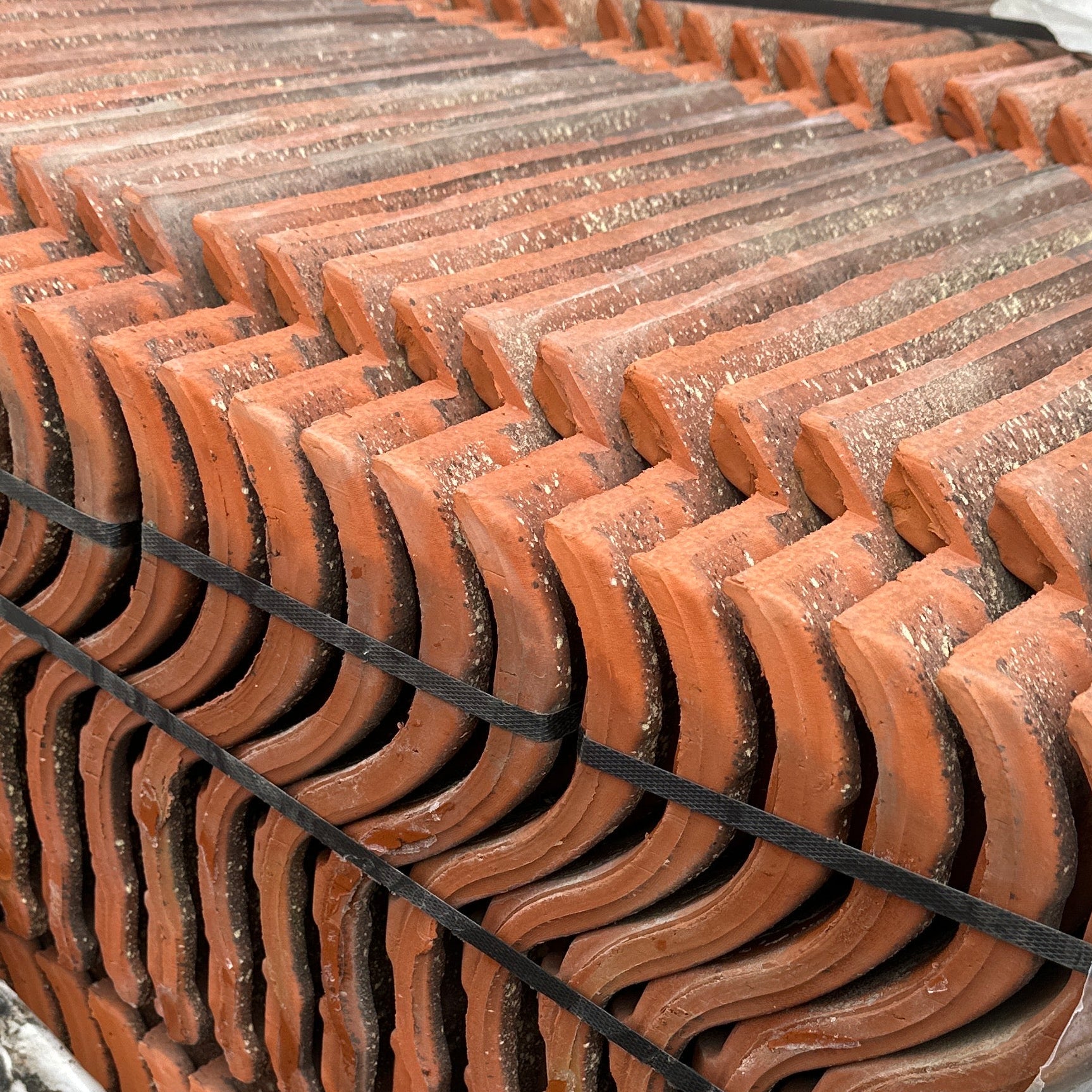 Stack of terracotta roof tiles on a wooden pallet with a wire mesh background