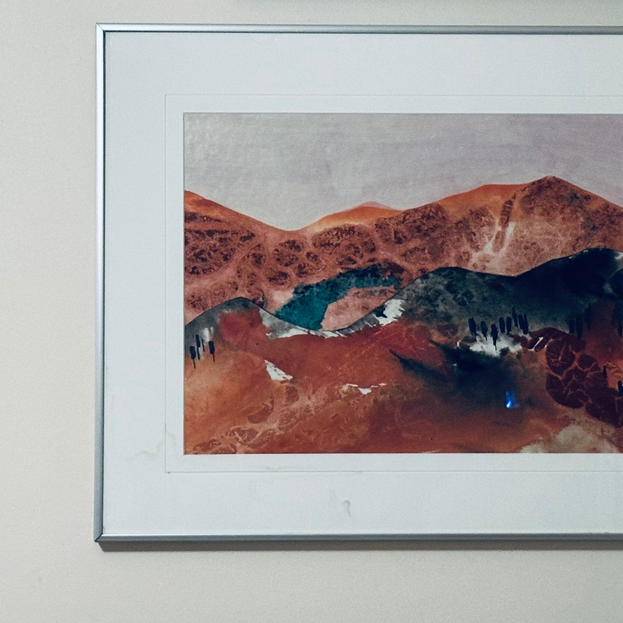 Framed artwork of a mountainous landscape in mixed media acrylic on a beige wall.