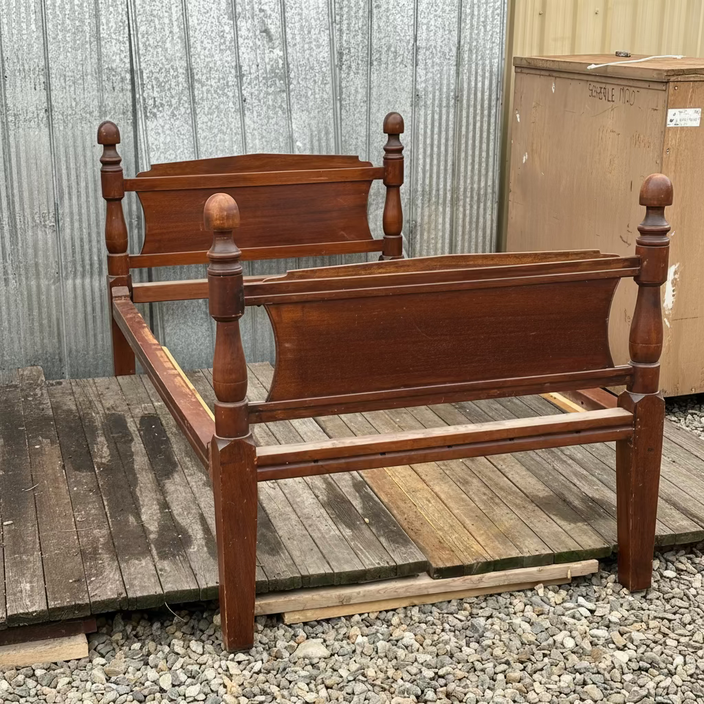Vintage Wooden bed frame on a gravel surface with a corrugated metal wall in the background