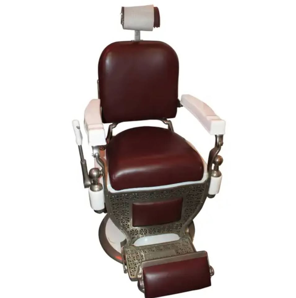 Vintage barber chair with burgundy leather seat and white armrests on a white background